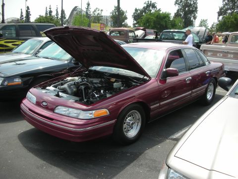 1992 Ford Crown Victoria - A maroon 1992 Ford Crown Victoria is displayed with its hood up, revealing the engine bay at an outdoor car show.