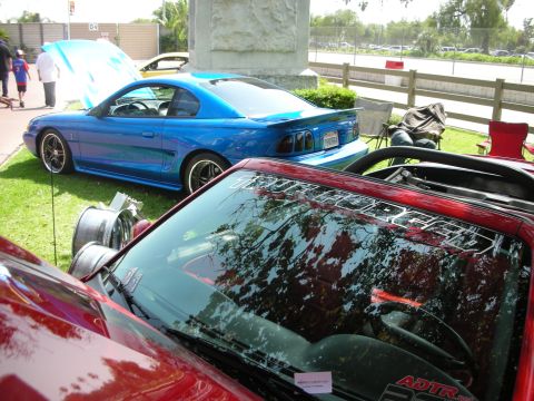 1992 Ford Crown Victoria - Two cars are parked on grass at an outdoor event, one blue Mustang and part of a red vehicle in the foreground.