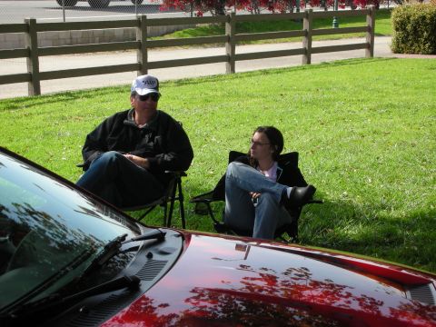 1992 Ford Crown Victoria - Two people relax on the grass next to a shiny red car.