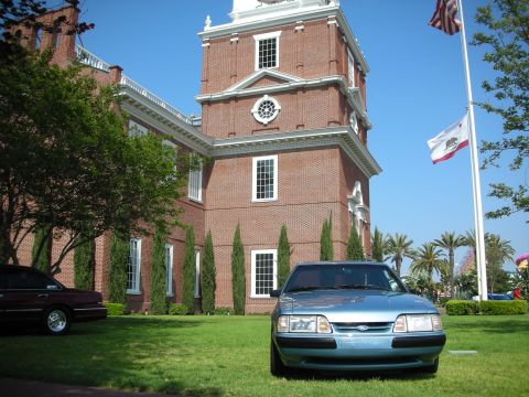 1992 Ford Crown Victoria - A blue sedan is parked on a lawn in front of a large brick building with flags flying.
