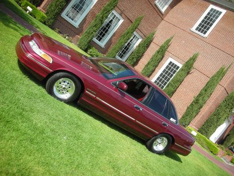 1992 Ford Crown Victoria - A maroon 1992 Ford Crown Victoria is parked on a grassy lawn in front of a brick building.