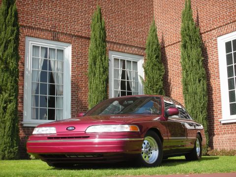 1992 Ford Crown Victoria - A maroon 1992 Ford Crown Victoria is parked on a grassy lawn in front of a brick building with large windows.