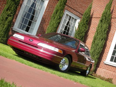 1992 Ford Crown Victoria - A maroon 1992 Ford Crown Victoria is angled on a lawn before a brick building with large windows.
