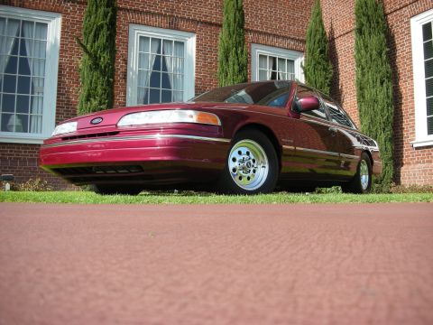 1992 Ford Crown Victoria - A maroon 1992 Ford Crown Victoria is parked in front of a brick building with manicured hedges.