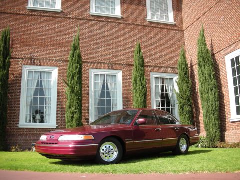 1992 Ford Crown Victoria - Maroon 1992 Ford Crown Victoria parked on grass in front of a brick building with tall windows.