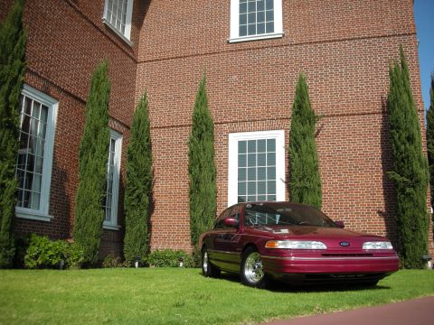 1992 Ford Crown Victoria - Maroon 1992 Ford Crown Victoria parked on grass in front of a brick building with tall windows.