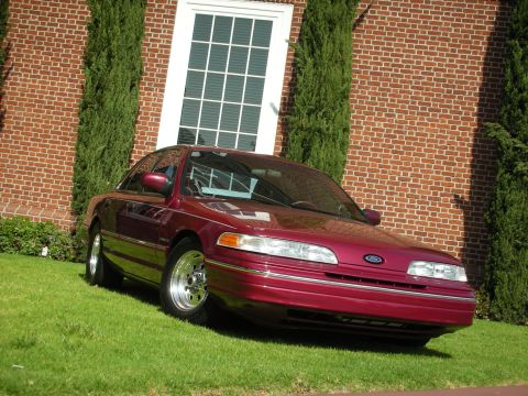 1992 Ford Crown Victoria - A maroon 1992 Ford Crown Victoria is parked on a grassy lawn in front of a brick building.