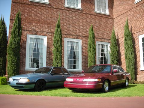 1992 Ford Crown Victoria - Two Ford vehicles, a Crown Victoria and a Mustang, are parked on the lawn in front of a brick building.