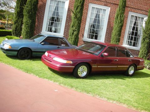 1992 Ford Crown Victoria - A maroon 1992 Ford Crown Victoria is parked on a lawn next to a blue coupe.