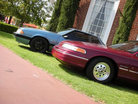 1992 Ford Crown Victoria - A maroon 1992 Ford Crown Victoria is parked on the grass next to a blue car in front of a brick building.