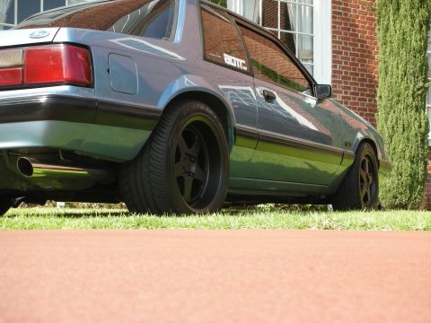 1992 Ford Crown Victoria - Side profile of a light blue Ford Mustang coupe with aftermarket black wheels and a "BOTIC" sticker.