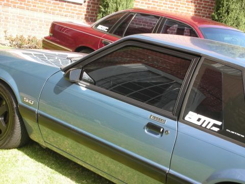 1992 Ford Crown Victoria - A blue 1992 Ford Mustang coupe is parked on grass, with a red sedan visible behind it.