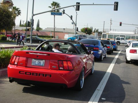 1992 Ford Crown Victoria - Red convertible Mustang Cobra in traffic, with other vehicles visible on a sunny day.