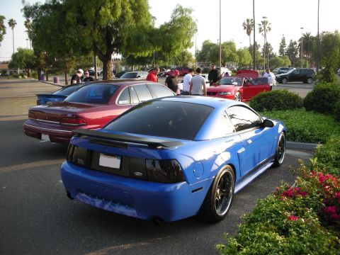 1992 Ford Crown Victoria - A blue Ford Mustang is parked in a lot with other vehicles and people milling around.