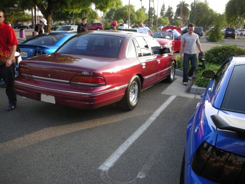 1992 Ford Crown Victoria - A red 1992 Ford Crown Victoria sedan is parked in a lot next to a blue car.
