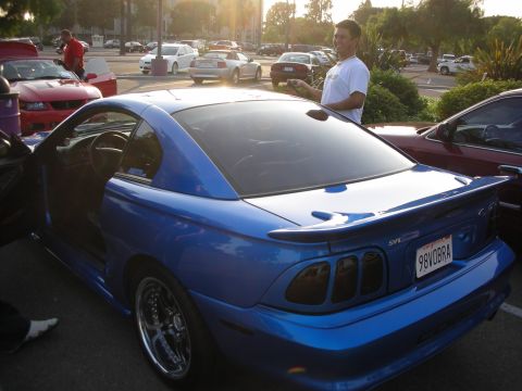 1992 Ford Crown Victoria - A blue 1998 SVT Cobra coupe is parked at a car show, showing off its rear spoiler and custom license plate.