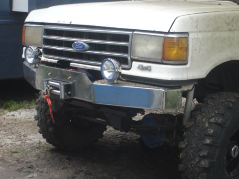 1989 Ford Bronco - Front view of a white Ford truck a chrome bumper with a winch and auxiliary lights.