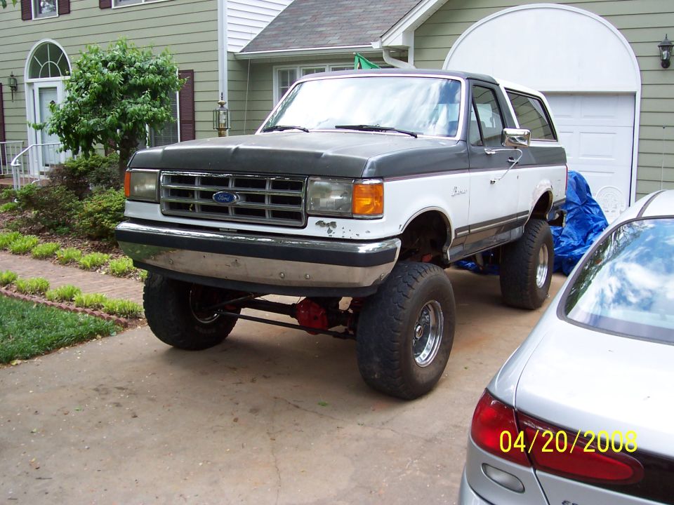 Lifted two-tone Ford Bronco with primer hood in a driveway