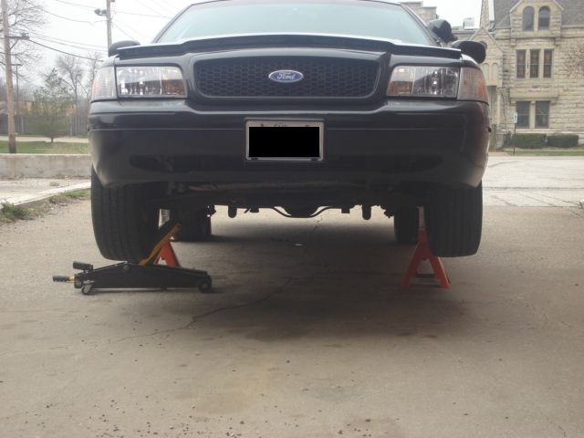 Front view of a black 2000 Ford Crown Victoria raised on jack stands with a floor jack visible