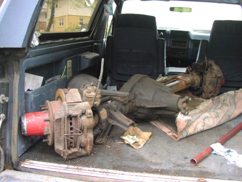 1986 Ford Bronco - Disassembled axles and brake components are stored in the cargo area of a vehicle.