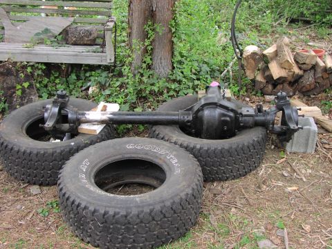 1986 Ford Bronco - A front axle assembly rests on tires outdoors, with visible branding from Goodyear tires.