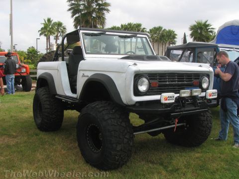 1968 Ford Mustang - A lifted white Ford Bronco sits on a grassy field next to other vehicles.