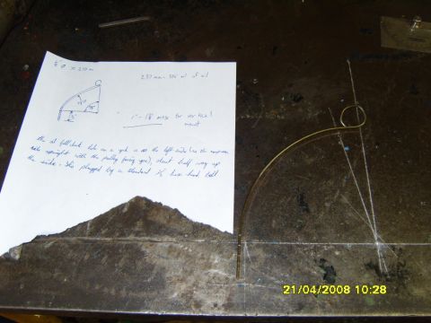 1989 Ford Bronco - A handwritten fabrication note sits on a steel workbench beside a bent brass rod dipstick tube laid over scribed layout lines. The page ske…