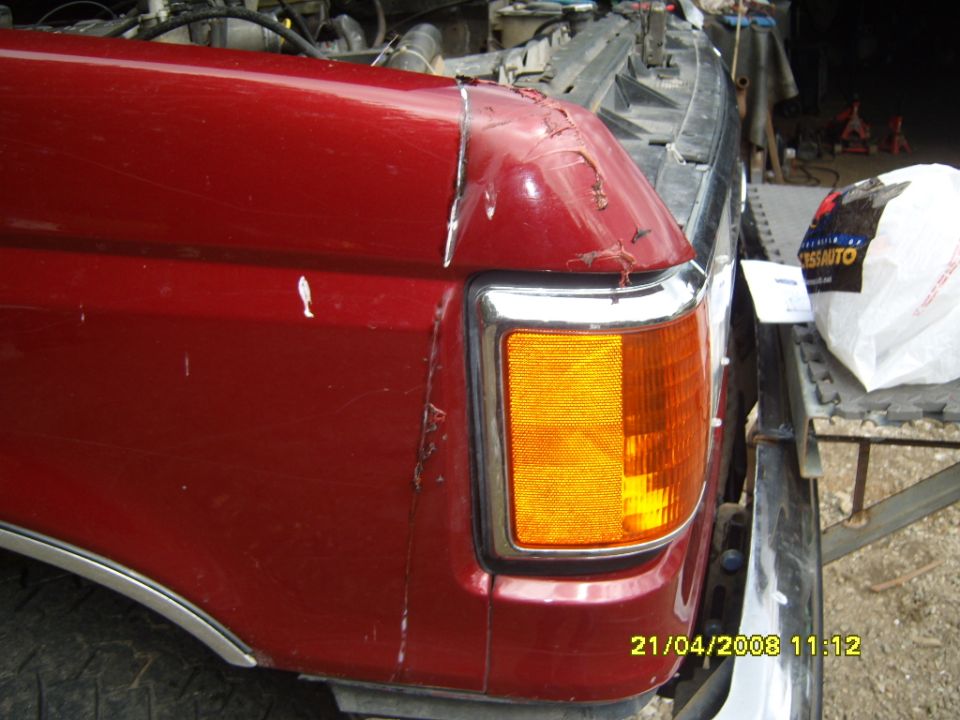 Damaged dark red fender corner with amber marker lamp and cracked paint