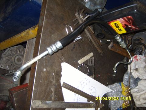 1989 Ford Bronco - A power steering hose lies on a workbench next to an oil container and various tools, suggesting a repair or installation in progress.
