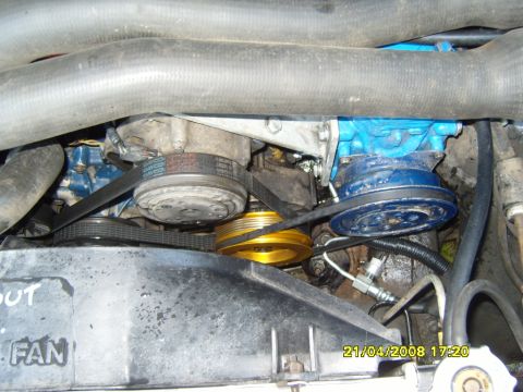 1989 Ford Bronco - Close-up of engine components including belts, pulleys, and a compressor, with a fan shroud visible.
