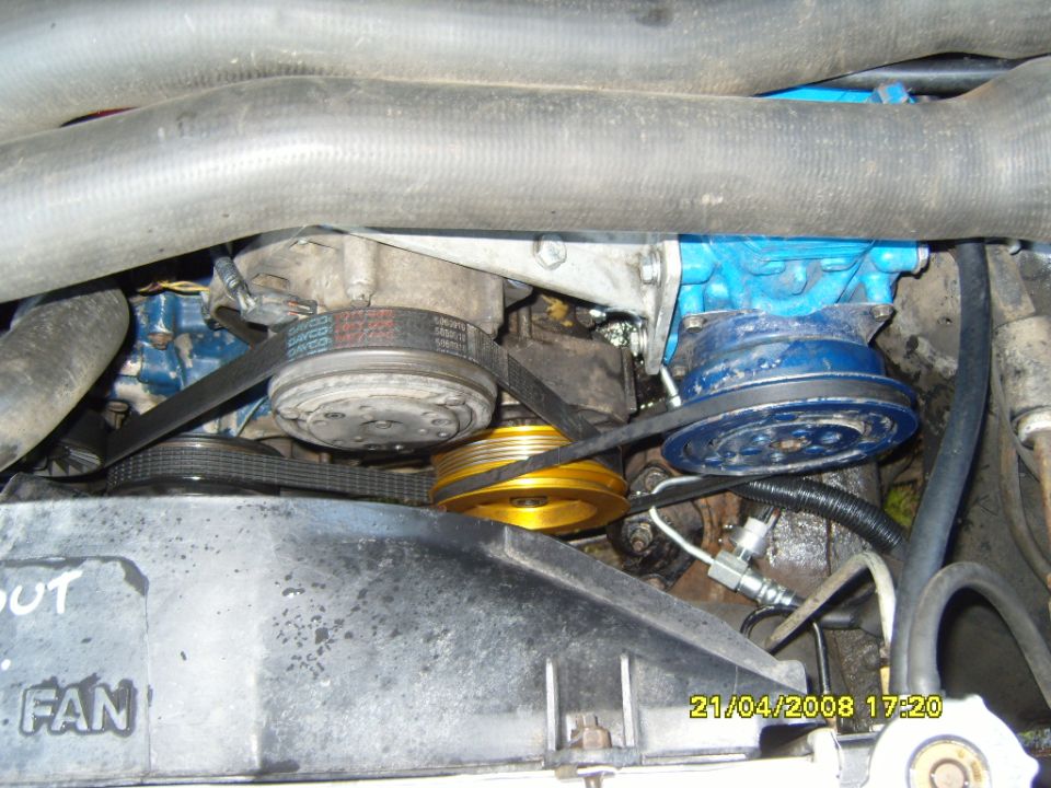Engine bay view showing belts, pulleys, compressor, and fan shroud with text 'OUT FAN'