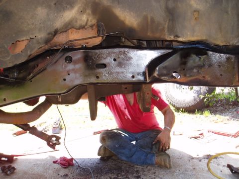1980 Ford Bronco - A person works on the frame and undercarriage of a vehicle, with parts of the exhaust and suspension visible.