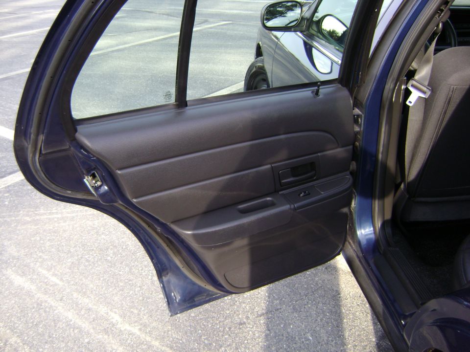 Dark blue sedan rear door interior, showing door panel and seatbelt. Another car is visible in the reflection