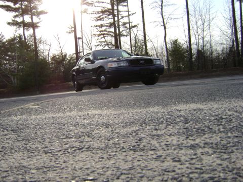 2001 Ford Crown Victoria - Black 2001 Ford Crown Victoria seen from a low angle on a paved road with trees in the background.