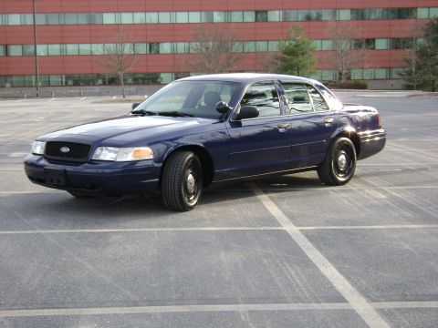 2001 Ford Crown Victoria - Dark blue 2001 Ford Crown Victoria sedan parked in a lot with a modern building in the background.