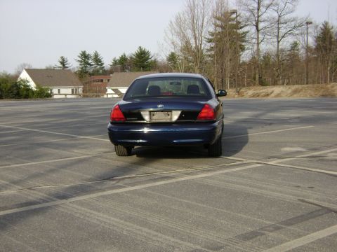 2001 Ford Crown Victoria - Rear view of a dark blue 2001 Ford Crown Victoria parked in a large, empty asphalt lot.