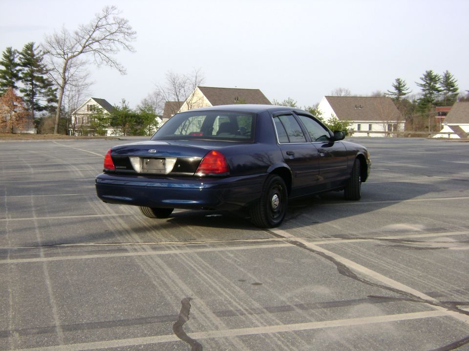 Dark blue Ford Crown Victoria parked in an empty lot. The car is seen from the rear-left