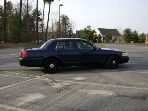 2001 Ford Crown Victoria - A dark blue 2001 Ford Crown Victoria sedan is parked in an empty lot.