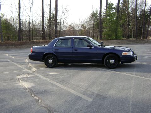 2001 Ford Crown Victoria - Side view of a dark blue 2001 Ford Crown Victoria parked in an empty lot with trees behind it.
