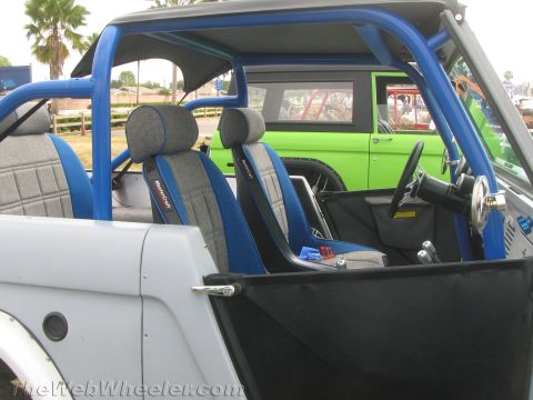 1968 Ford Mustang - The interior of a modified Ford Bronco features racing seats and a prominent blue roll cage, with another Bronco in the background.