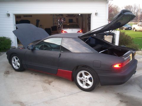 1993 Ford Probe - A matte black 1993 Ford Probe with its hood and trunk open is parked in a driveway with a garage in the background.