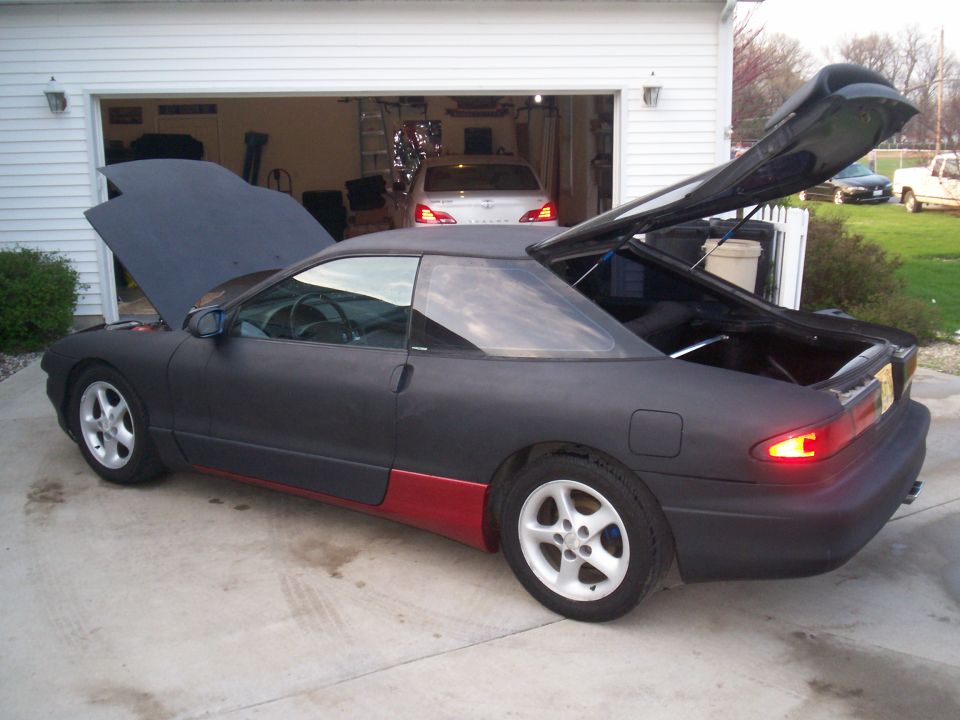 Matte black 1993 Ford Probe with red lower body panels, hood and trunk open, parked in driveway