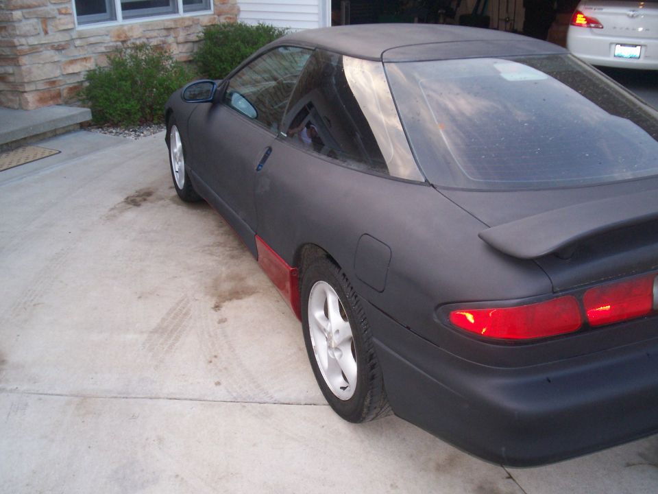 1993 Ford Probe with matte black paint and red lower body panels, parked on a concrete driveway
