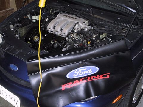 1996 Ford Taurus - The engine bay of a blue 1996 Ford Taurus is visible, covered by a black Ford Racing engine cover.