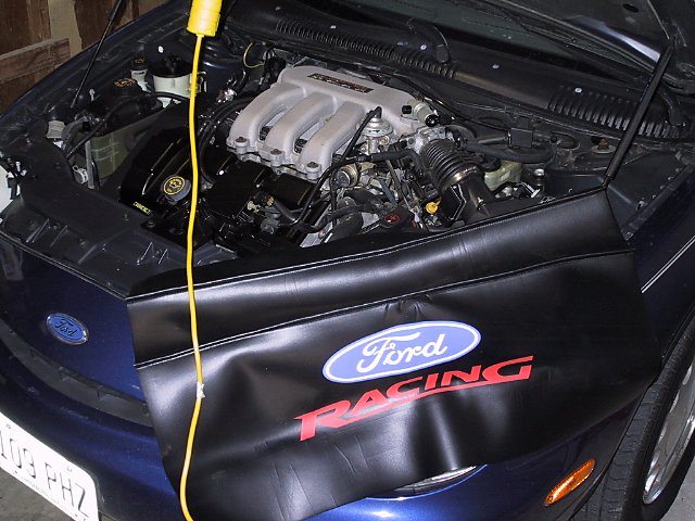 Blue Ford Taurus engine bay with a black Ford Racing cover over the engine