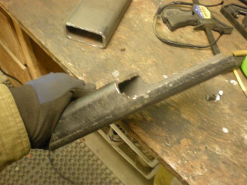 1993 Ford Bronco - A metal tube is being held and examined on a workbench, with tools and other metal pieces visible.