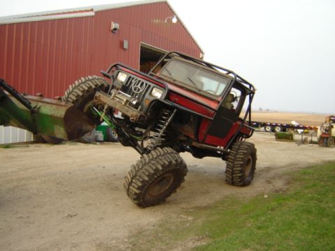1992 Ford Bronco - Modified Jeep Wrangler with a front loader attached, parked on a dirt surface near a red barn.