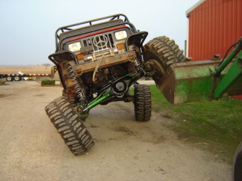 1992 Ford Bronco - A heavily modified off-road vehicle is precariously balanced, being lifted by a tractor's front loader.