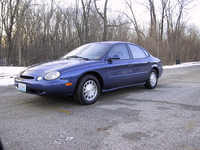 Blue 1996 Ford Taurus sedan parked on asphalt with snow in the background