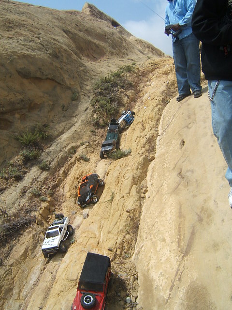 1988 Ford Bronco - RC off-road vehicles tackle a challenging rocky terrain, controlled by people on the ridge above.
